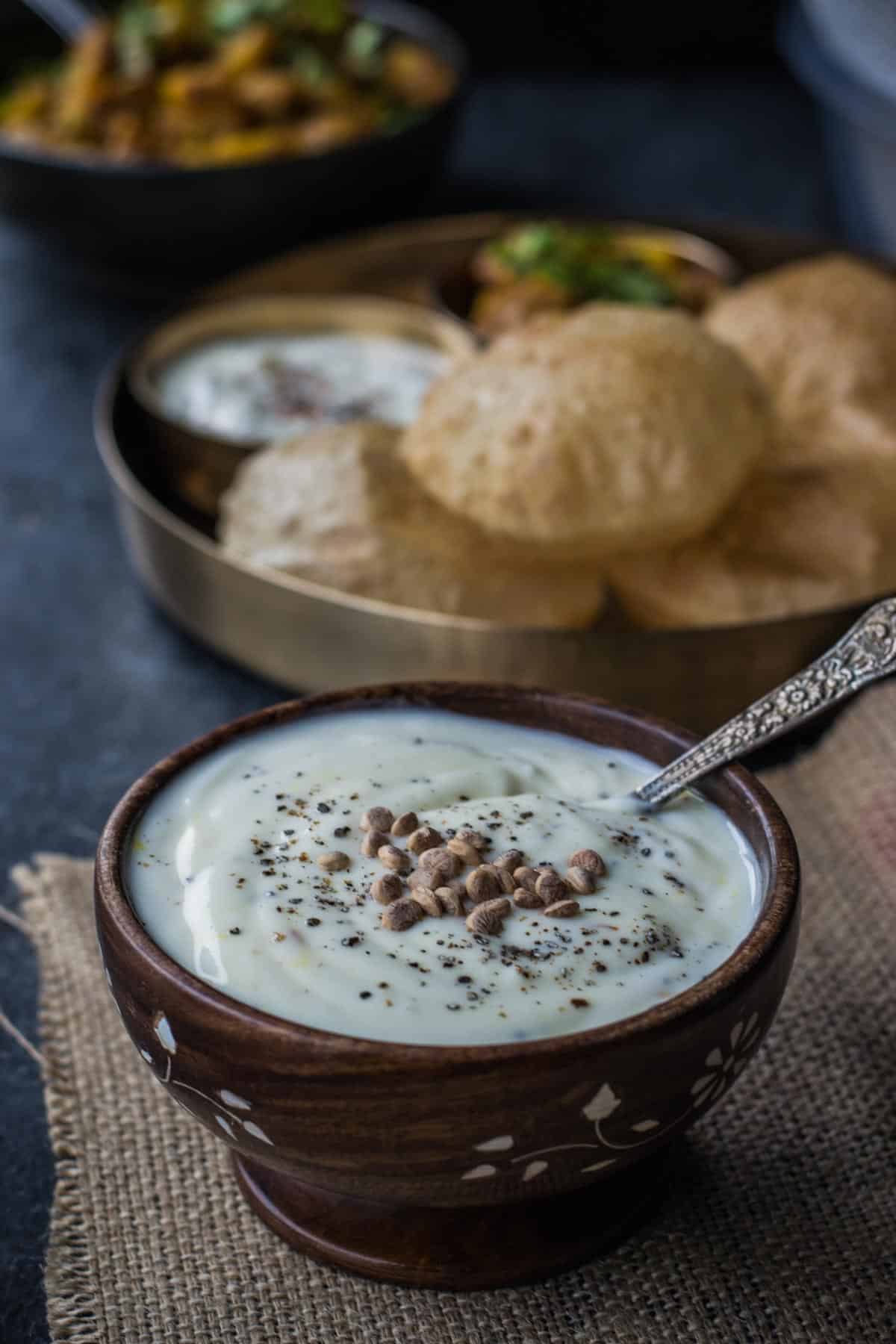 Shrikhand served in a wooden bowl along with pooris served in a golden plate. 