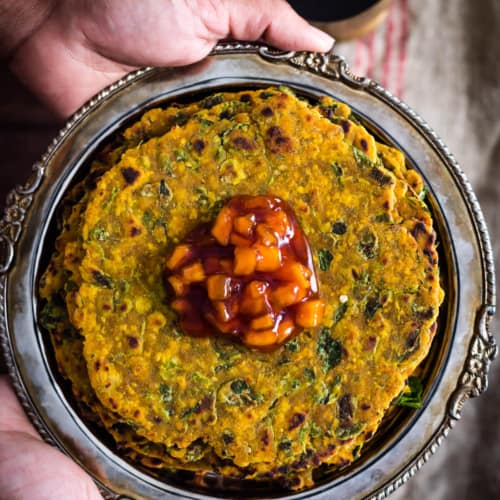 Methi thepla served in a metal plate with chundo on top