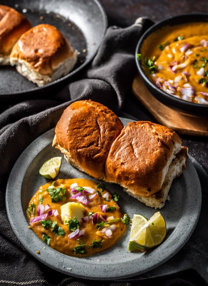 Pav bhaji served with a silver of butter, finely chopped onions, crispy pav and lemon wedges
