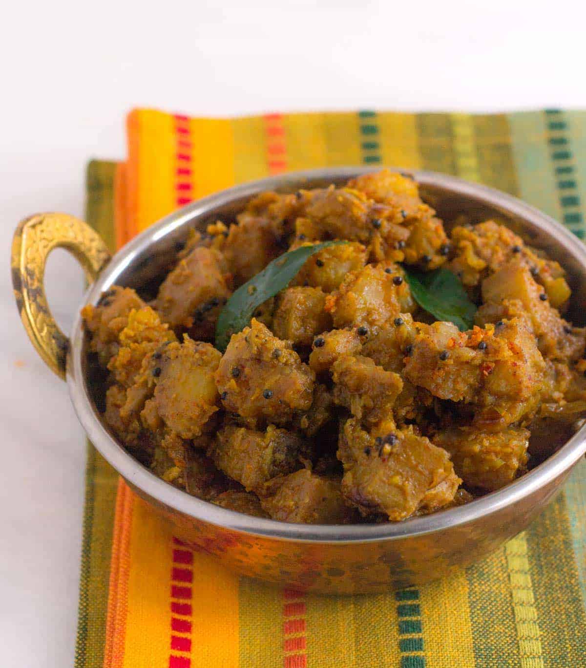 Kaccha kela sabzi served in a metal bowl garnished with curry leaves