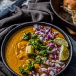 Instant Pot Pav bhaji served with a silver of butter, finely chopped onions, and lemon wedges in a black bowl