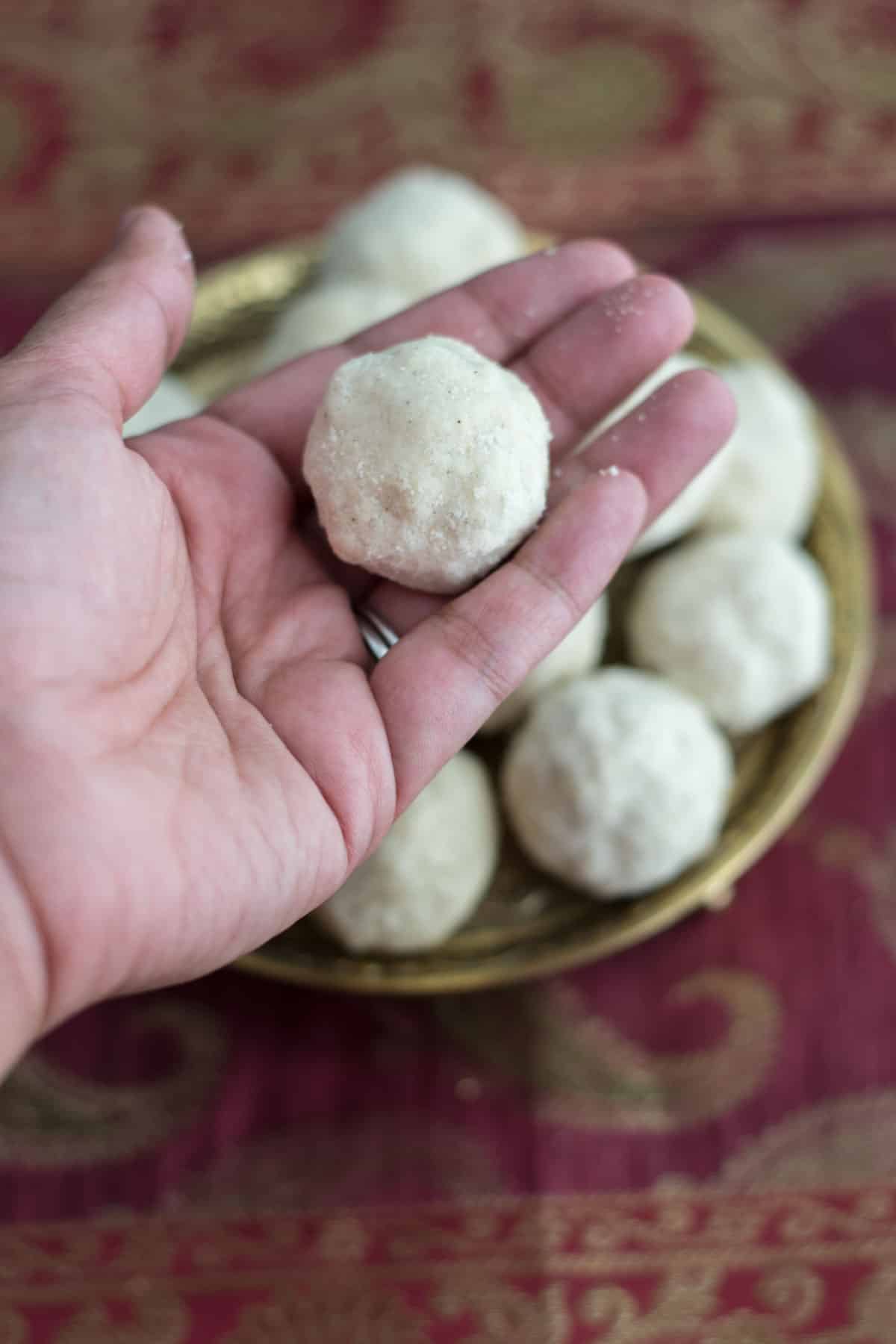 Rolled rava laddoo held in a hand over a stack of laddoos