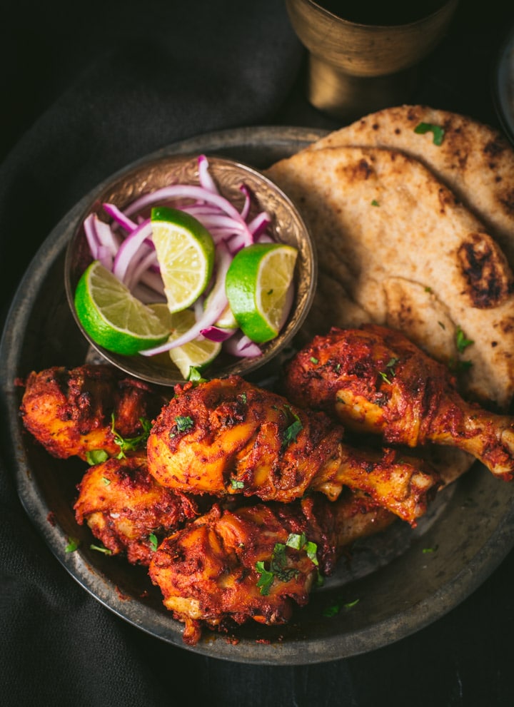 Tandoori chicken is served with a side of lemon wedges, sliced onions and naan