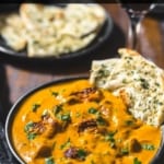 Chicken Tikka Masala served in a black bowl with garlic naan dipped in it
