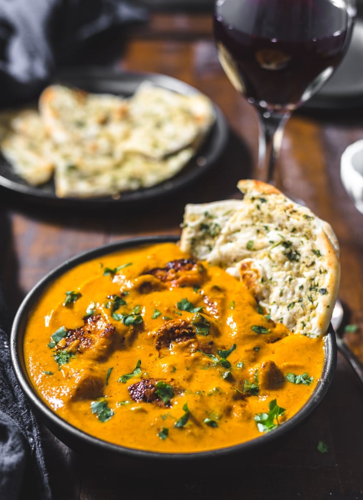 Chicken Tikka Masala served in a black bowl with garlic naan dipped in it