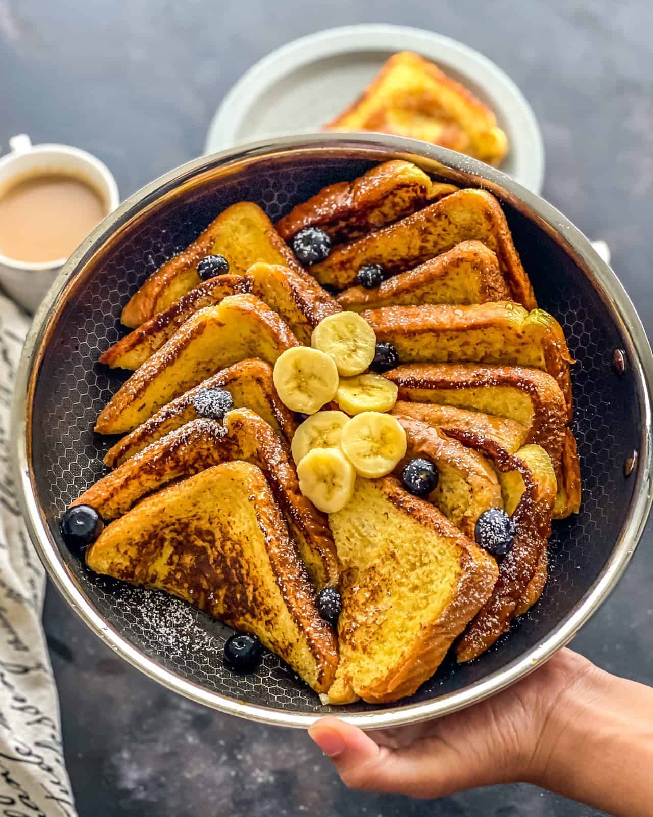 A silver pan with cut slices of french toast topped with blueberries and slices of banana.