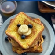 A blue plate with slices of french toast stacked on top and blueberries and bananas to garnish with the words easy and fluffy french toast on the top.