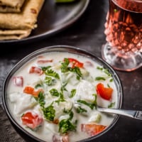 Cucumber tomato raita served in a black bowl and is accompanied by rotis and a glass of raspberry lemonade