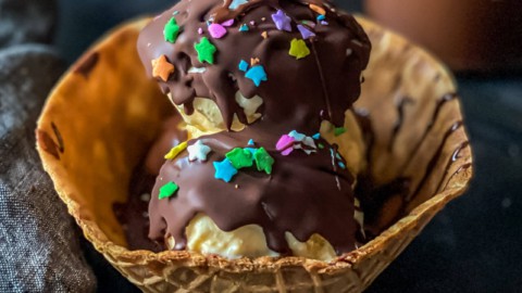 A waffle bowl with scoops of vanilla ice cream topped with homemade magic shell and sprinkles.