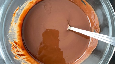 Fully melted and stirred together chocolate magic shell sauce in a glass bowl with a silver spoon.