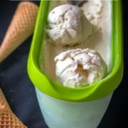 Vanilla ice cream in a tupperware with two rolled scoops and an ice cream scoop in the back and 3 ice cream cones on the right and the words vanilla ice cream, eggless, 3-ingredient, and no-churn at the top.