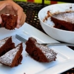 A hand holding a piece of cake. Chocolate cake pieces served on a white plate.