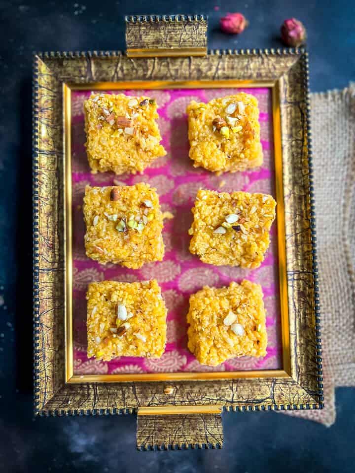 6 pieces of mango kalakand placed in a dark pink and golden tray