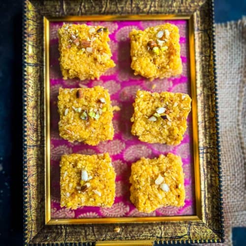 6 pieces of mango kalakand placed on a pink and golden tray