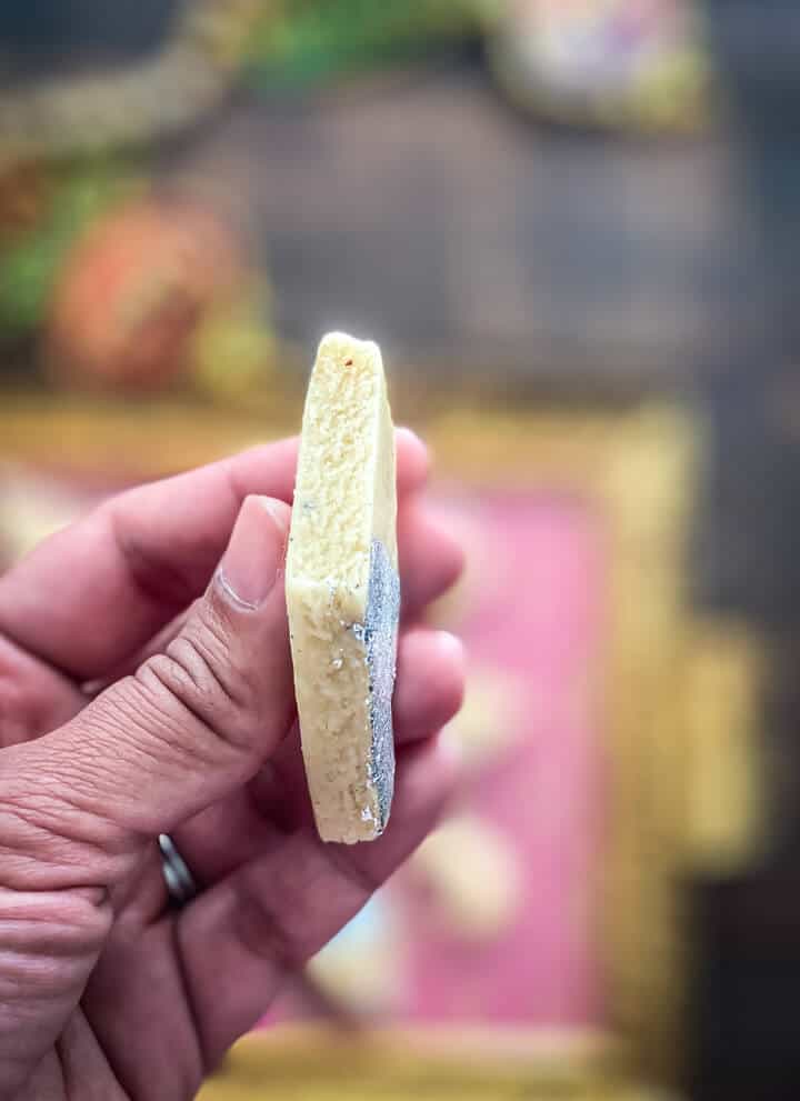 A hand holding a piece of kaju katli