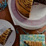 Zebra cake on a cake stand with a white plate with a slice of cake on the side.