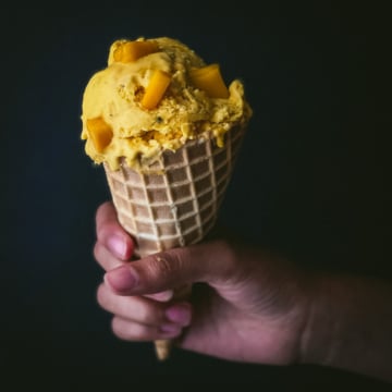 A hand holding a cone filled with mango ice cream