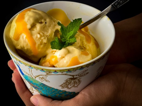 A hand holding a bowl of mango ice cream topped with mango puree
