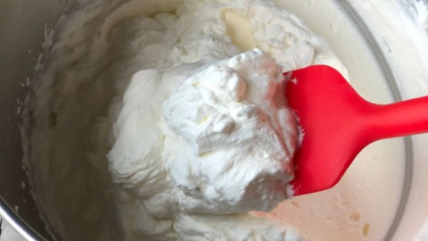 A red spatula scooping thick whipped cream