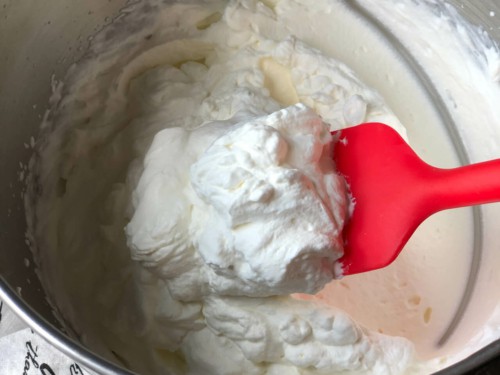 A red spatula scooping thick whipped cream