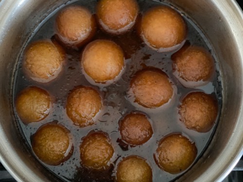 Gulab jamun soaking in a silver bowl of sugar syrup.