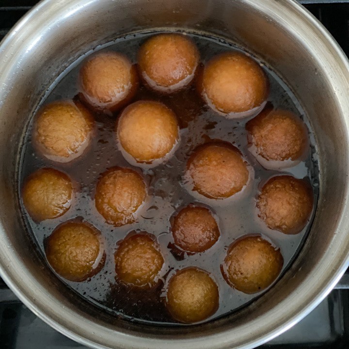 Gulab jamun soaking in a silver bowl of sugar syrup.