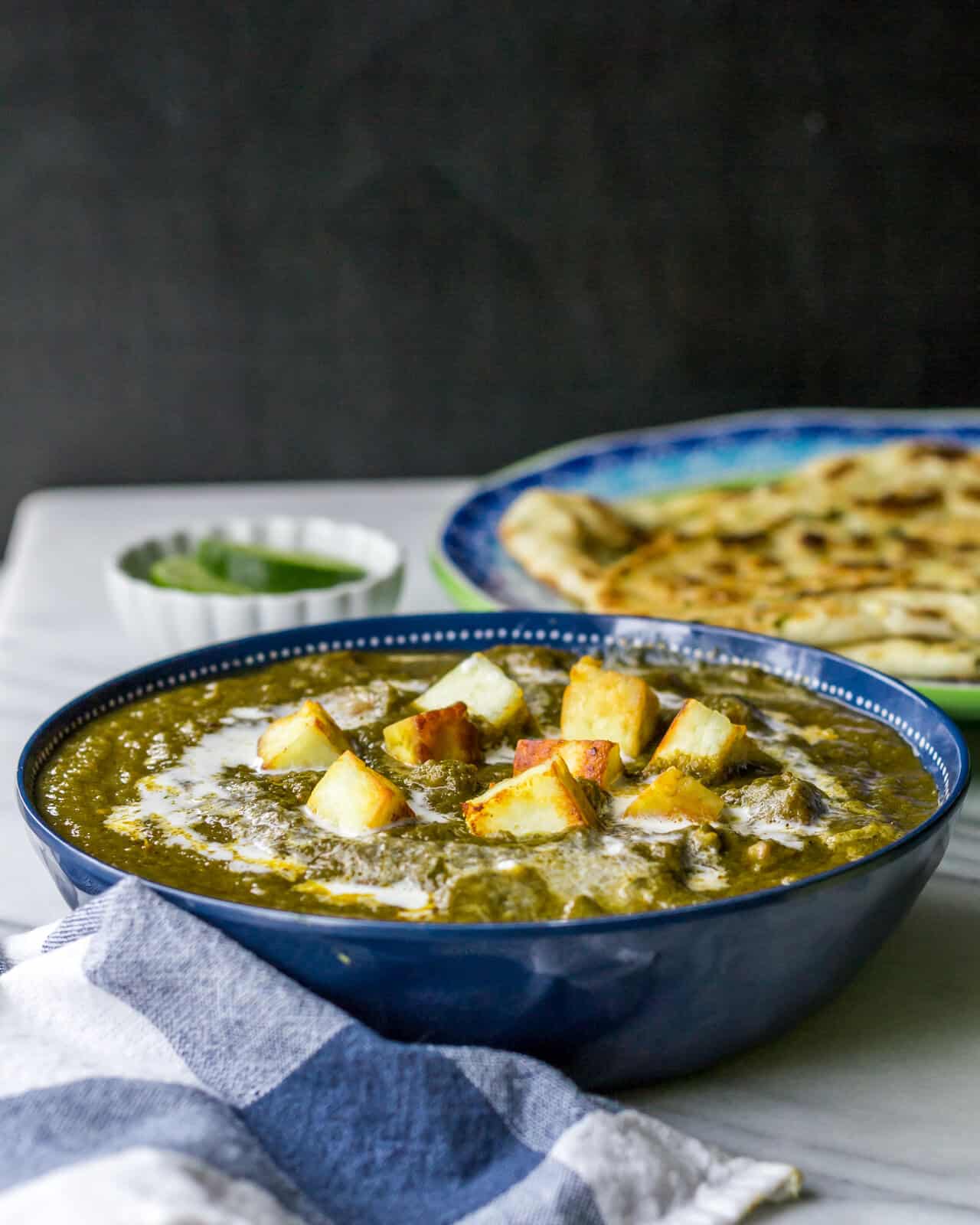 Restaurant style Palak Paneer served in a blue bowl with naan and lemon on the side