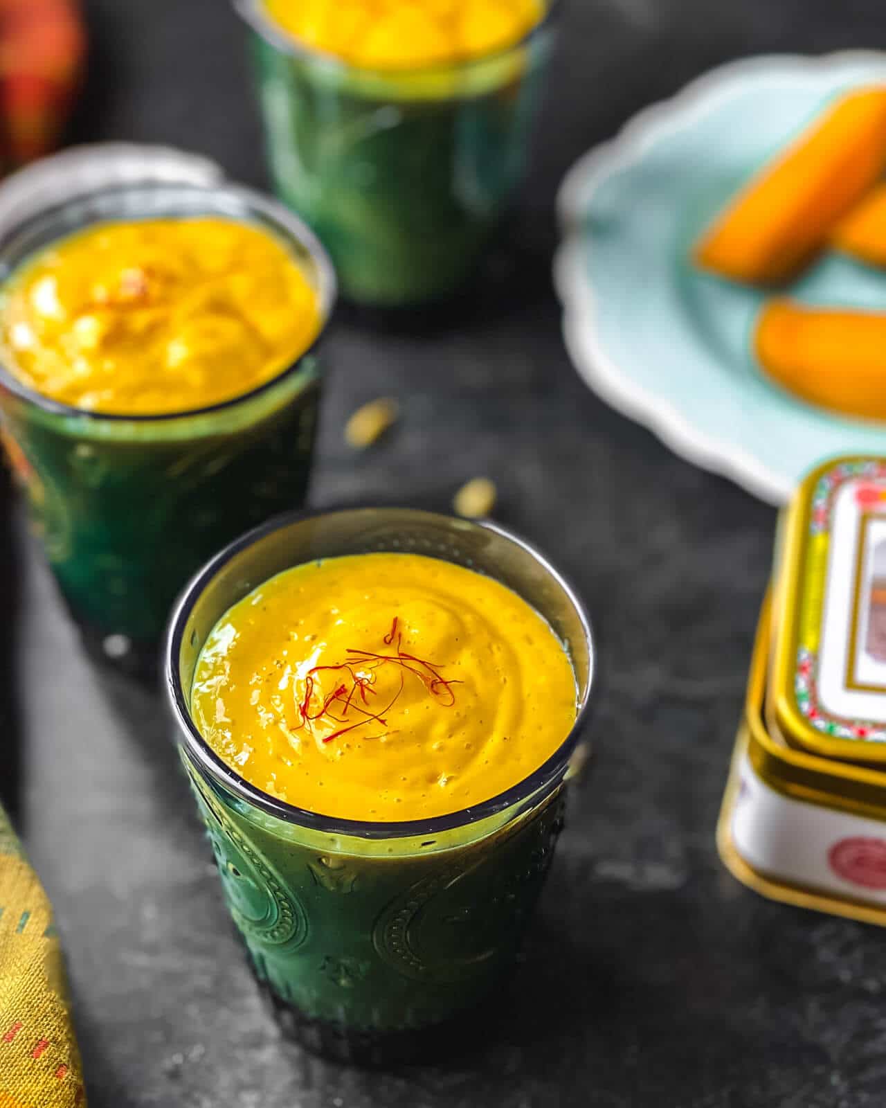 Two glasses of Mango lassi served with a plate of mango slices