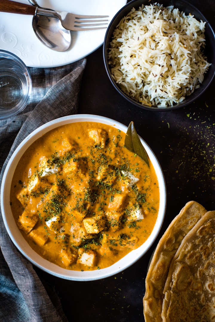 Paneer Makhani served in a white bowl accompanied by parathas and jeera rice