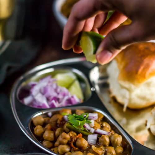 Chana masala served with a side of pav, onions and sprinkled with lime juice
