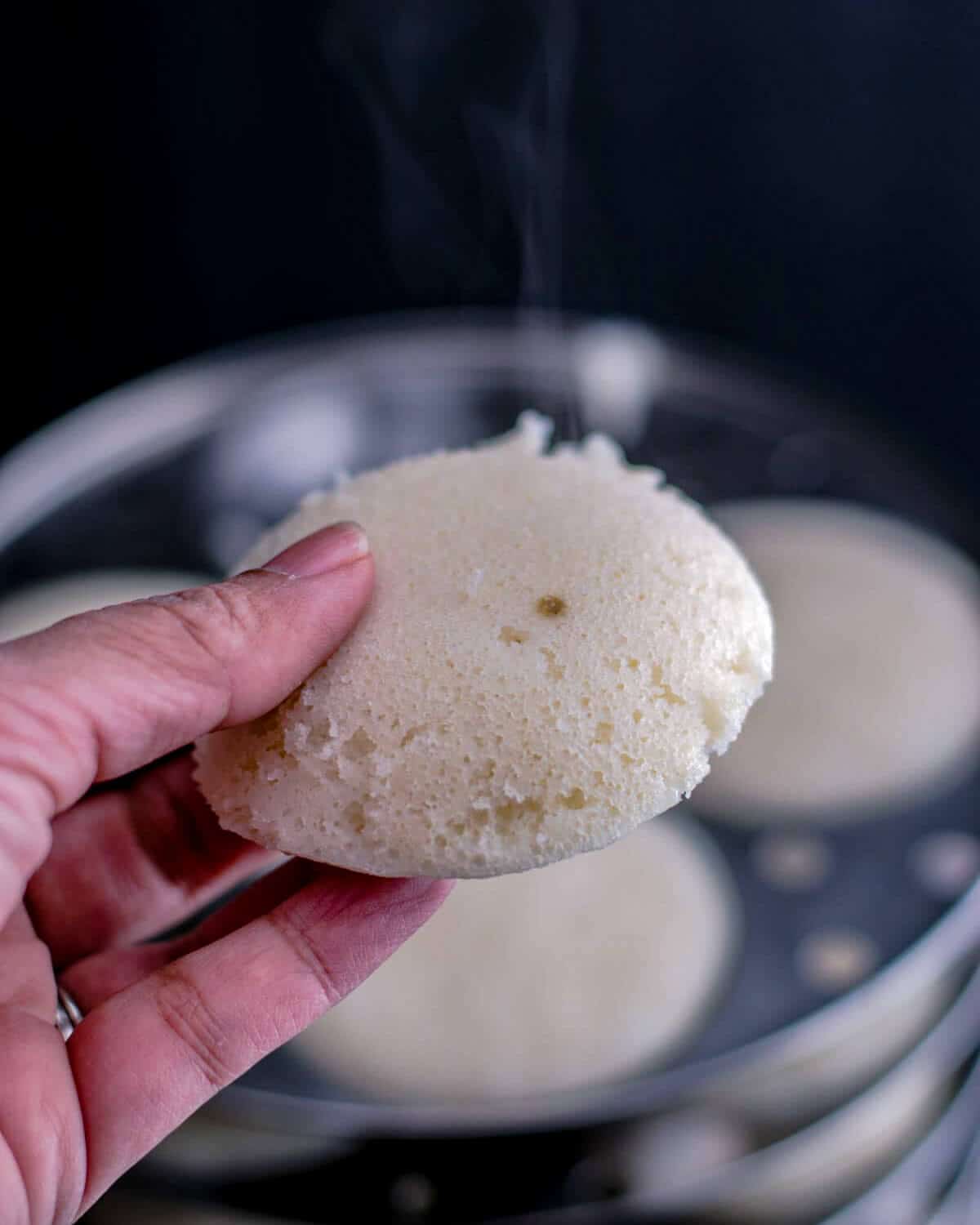 A hand holding a steaming hot idli