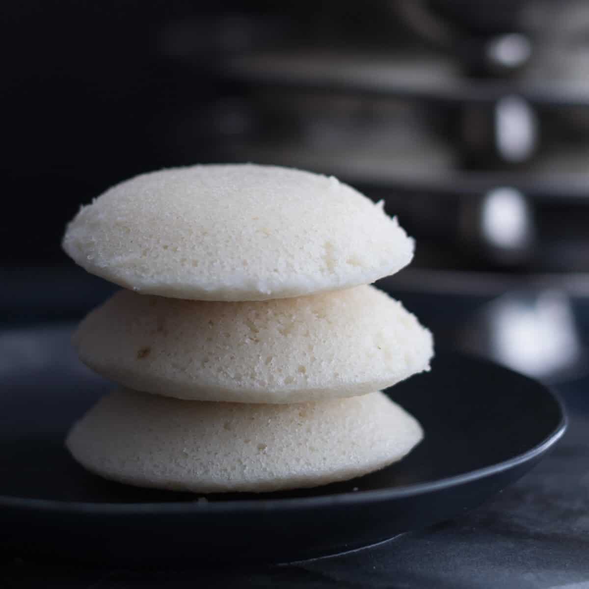 A stack of 3 spongy idlis kept on a black plate