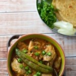Achari chicken served in a green bowl topped with green chili 