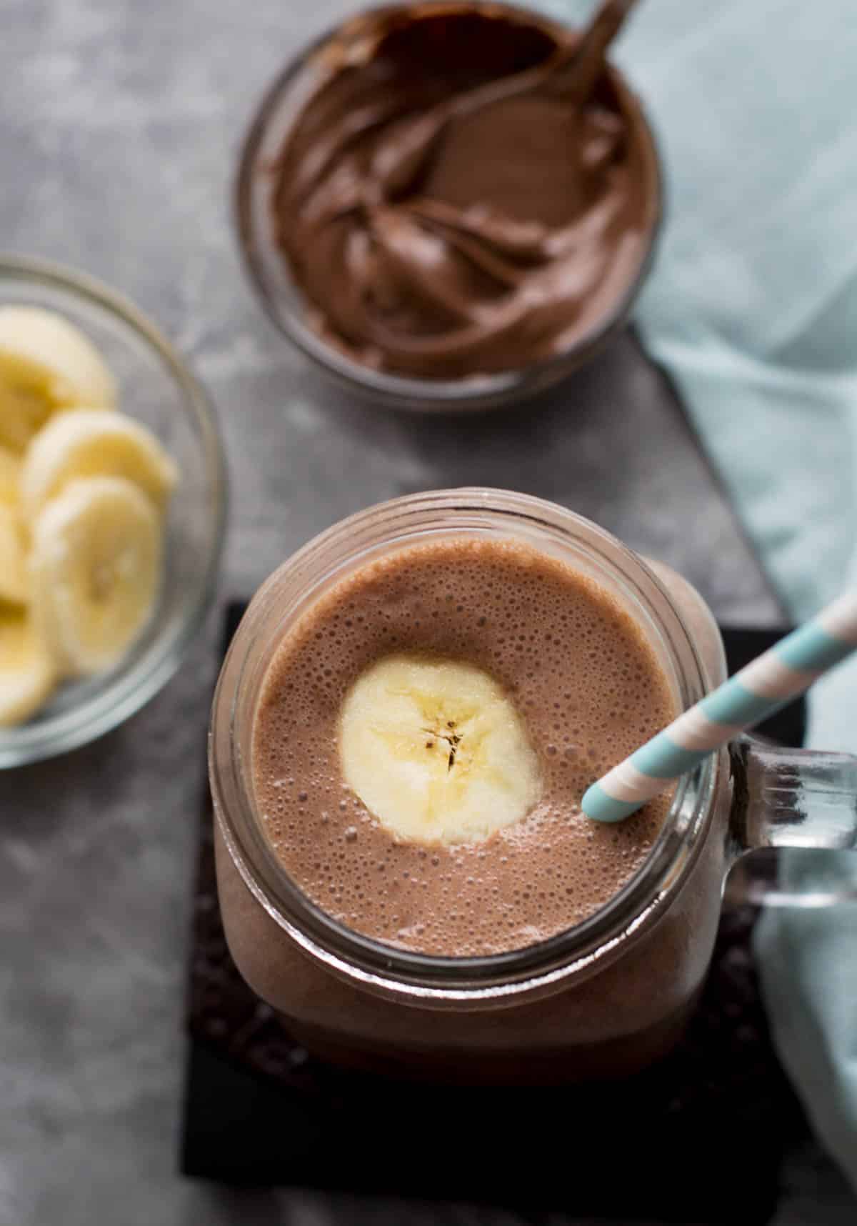 Overhead shot of banana nutella smoothie in a mason jar with a striped blue and white straw