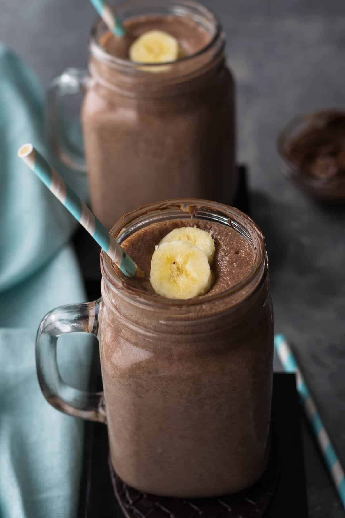 Two mason jars with a blue straw in both filled with banana nutella smoothie