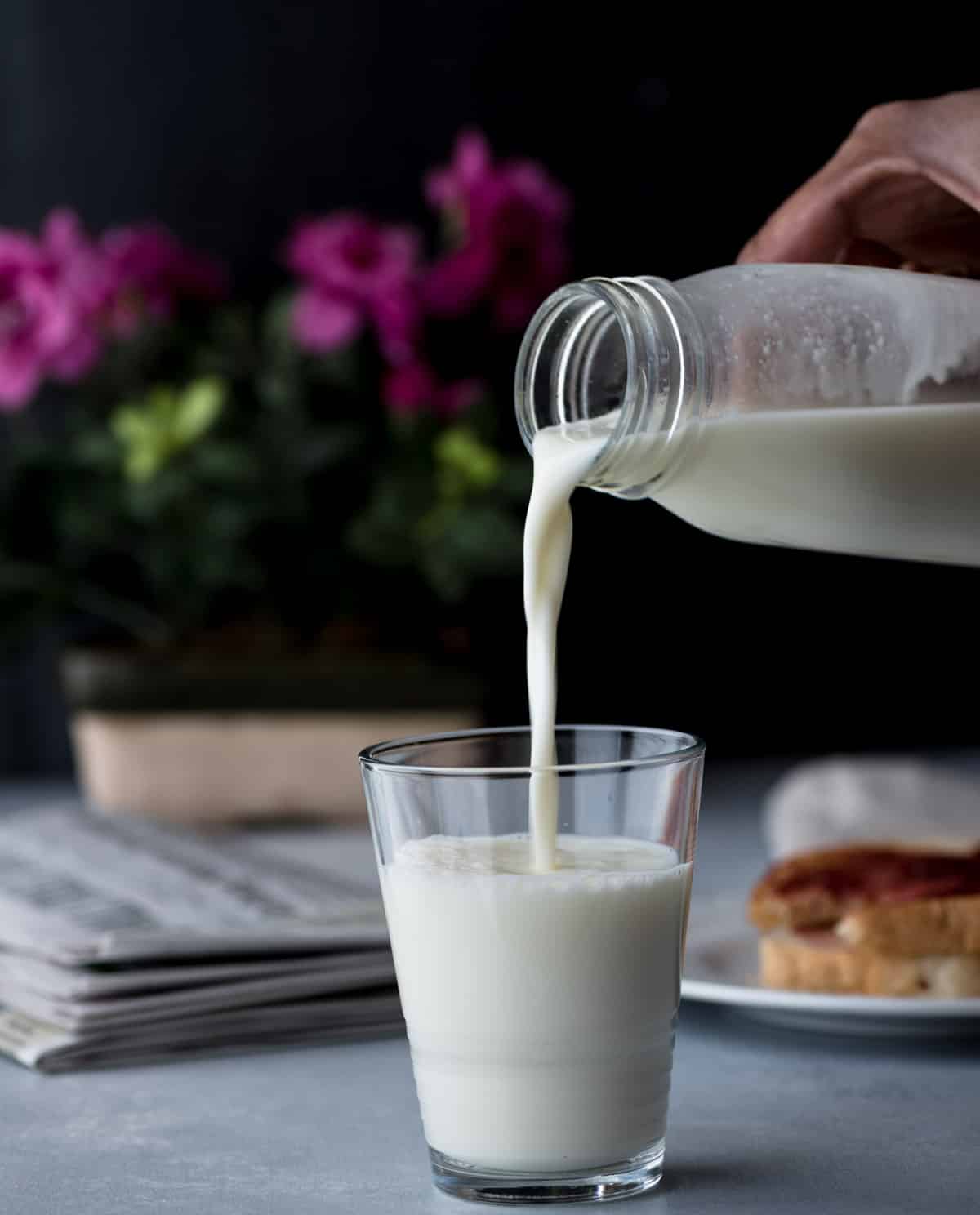 A hand pouring milk from a bottle into a glass