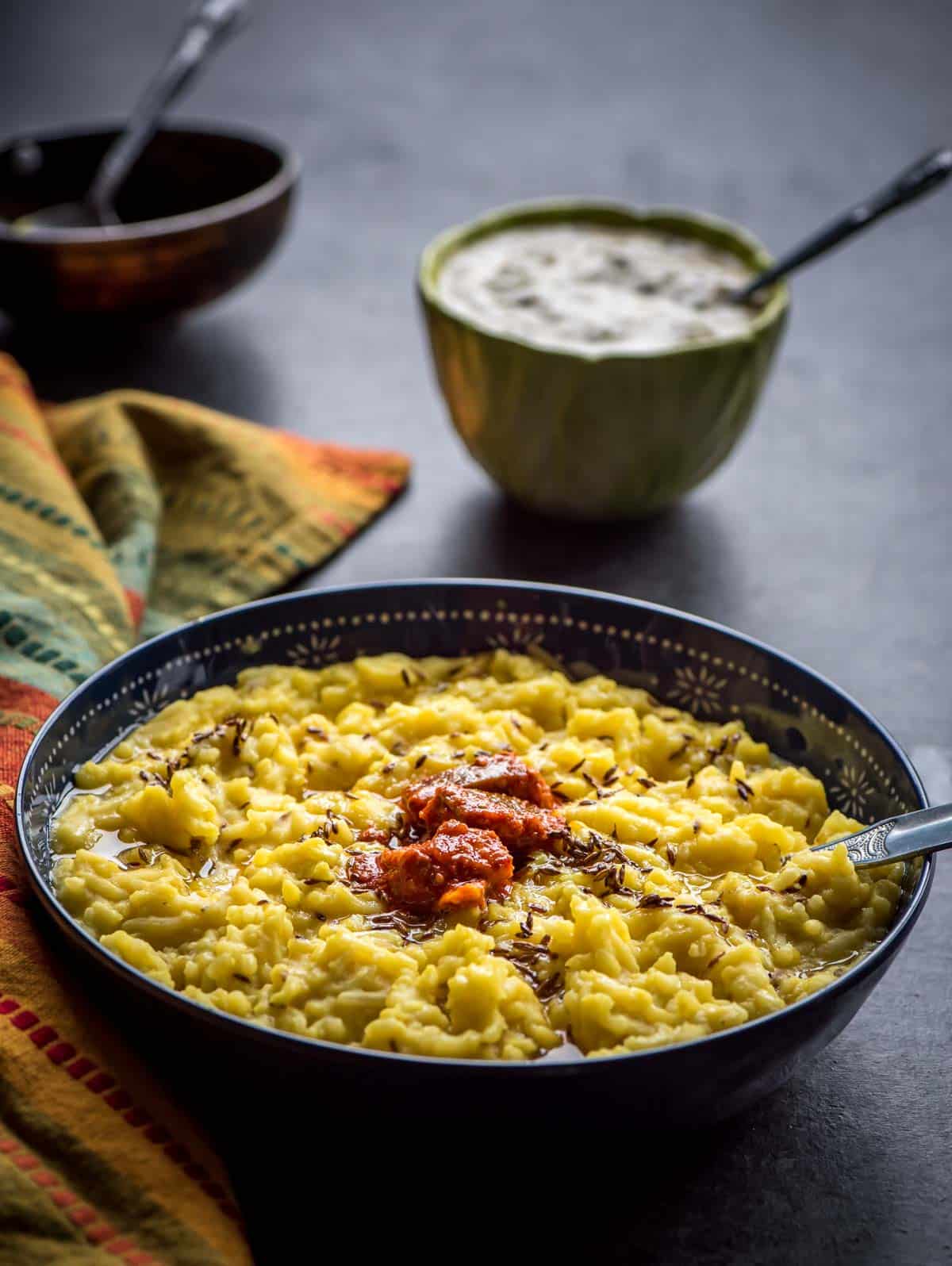 Moong dal khichdi served with raita and tempering in a blue bowl