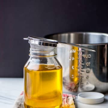 Ghee in glass bottle with strainer and a steel pot on the side