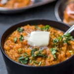 Pav bhaji served in a black bowl garnished with cilantro and a dollop of butter