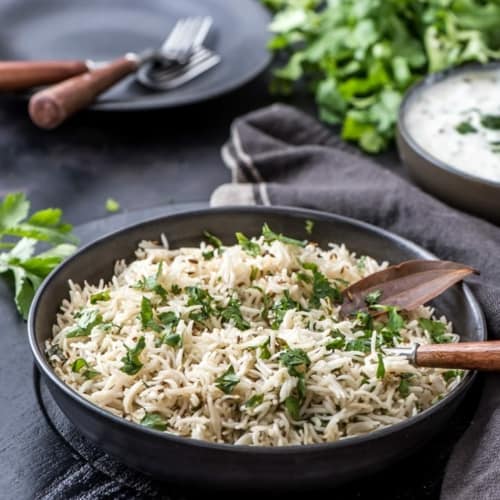 Cumin rice served in a black bowl garnished with cilantro