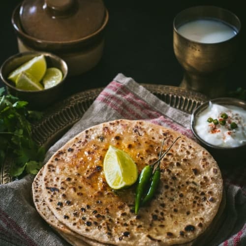 Paneer paratha served with a side of yogurt, lemon and green chilies
