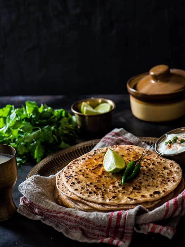 Paneer paratha served with yogurt and lime slices along with green chilies