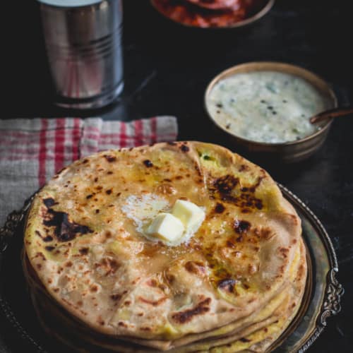 Aloo paratha served with lassi, pickle, raita and dollop of butter