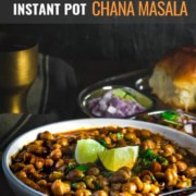Chana masala served in a white bowl with side of lemon. On the side is a steel plate with pav and some more chana masala served with onions and lime wedges.