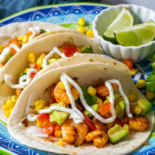 3 Shrimp tacos are lined up on a blue plate with greek yogurt dressing on top