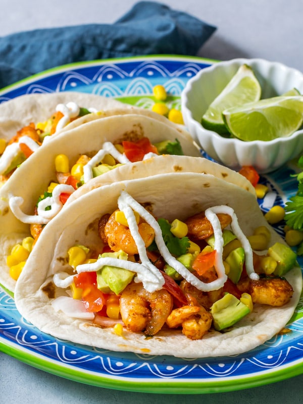 3 Shrimp tacos are lined up on a blue plate with greek yogurt dressing on top