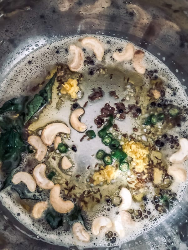 An overhead shot of the Instant Pot Steel Insert with cashews being fried in ghee along with cumin seeds, ginger, green chilies, black peppercorns and asafoetida