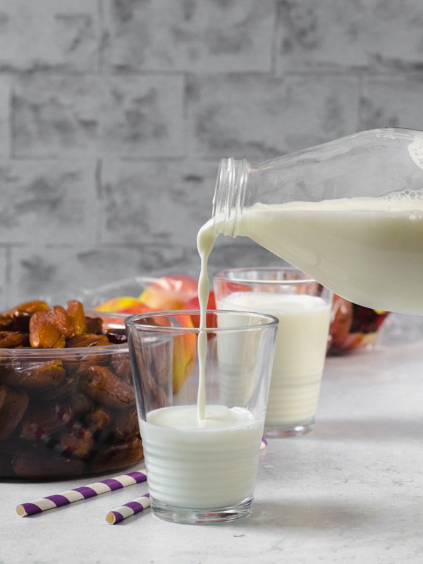 Milk is being poured from a glass bottle into a glass. A box of dates is next to it. 