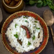 Curd rice served in a metallic gold and red bowl accompanied by pickle in a ceramic brown bowl with coriander on the side