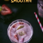An overhead shot of strawberry banana smoothie garnished with chopped bananas and strawberries in two glass containers and placed on a wooden bowl. There are two red and white straws on the side.